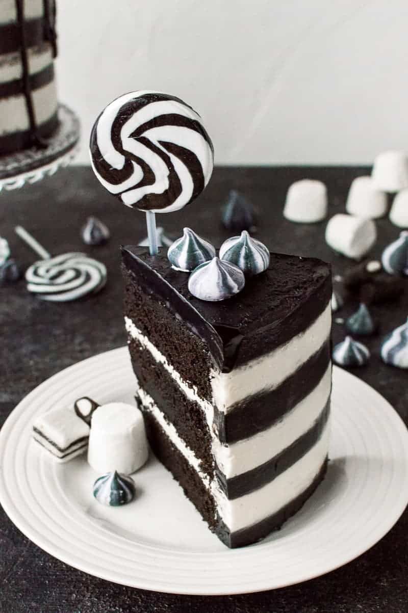 A slice of black and whitestriped monochrome chocolate and vanilla cake topped with a lollipop.
