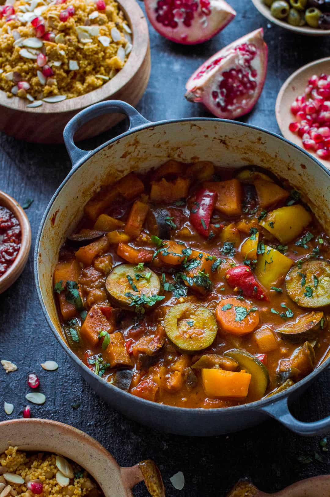Angled shot of vegan vegetable tagine in a casserole dish with couscous and pomegranate.