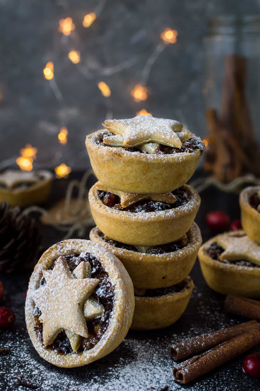 Photograph of a stack of lower calorie vegan mince pies with fairy lights in the background.