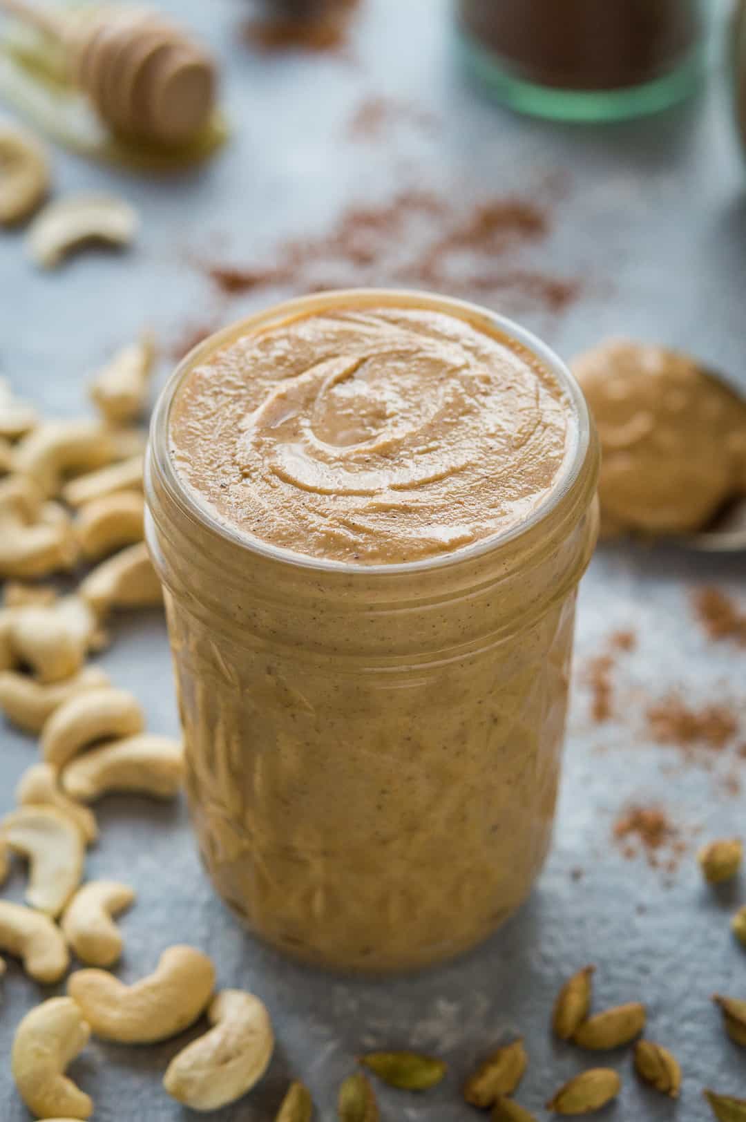 Chai spiced cashew butter in a glass jar surrounded by ingredients