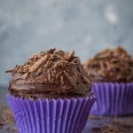 Two vegan chocolate cupcakes in purple cake cases.