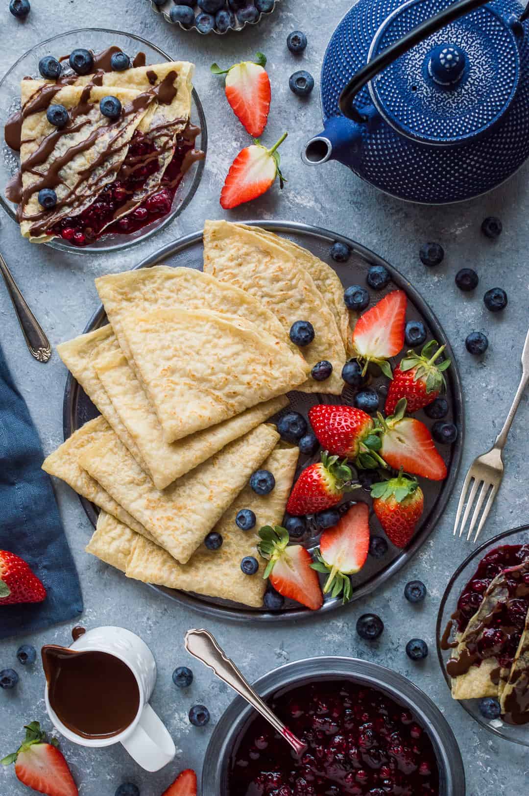 Top down shot of a breakfast spread of vegan pancakes with berries, chocolate sauce and berry compote.