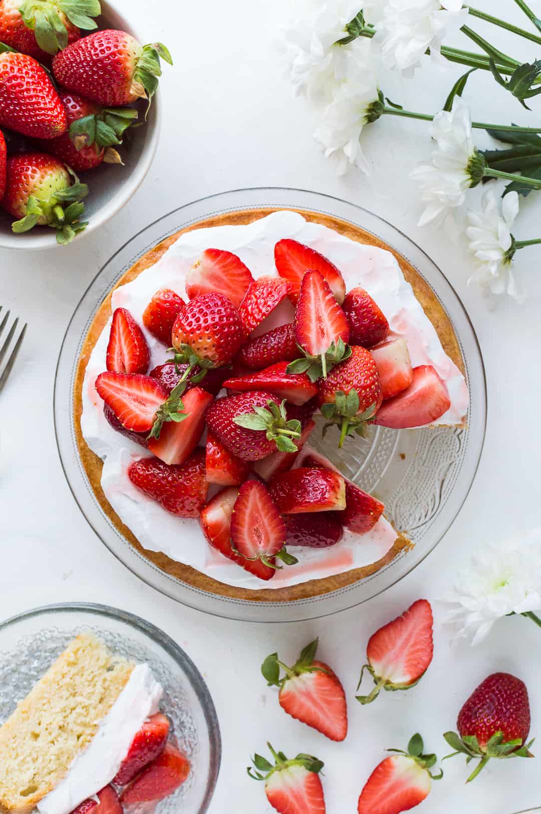 top down shot of vegan lemon almond cake topped with coconut cream and strawberries with a slice taken out.