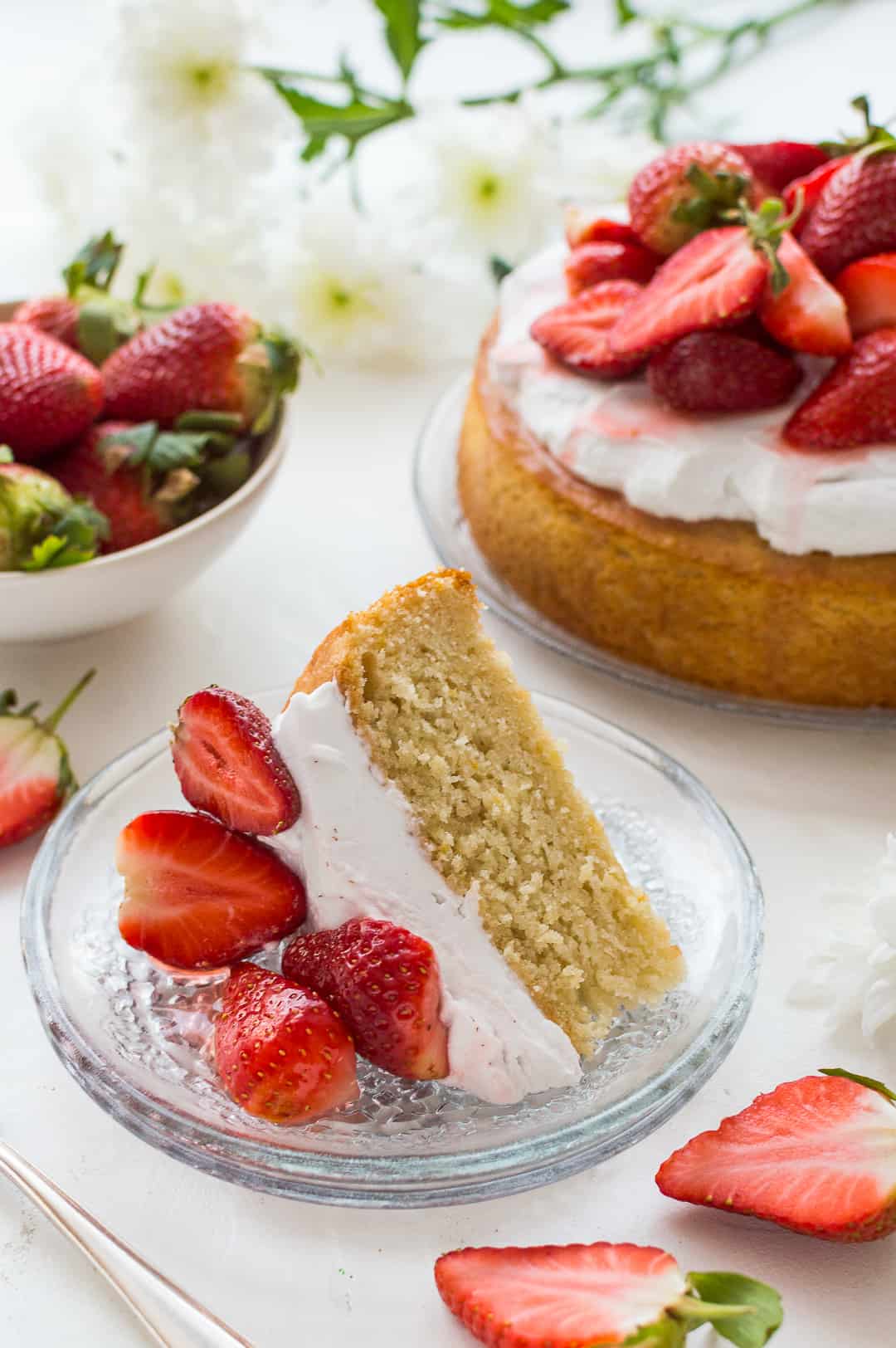 A slice of vegan lemon and almond cake with coconut whipped cream and strawberries.