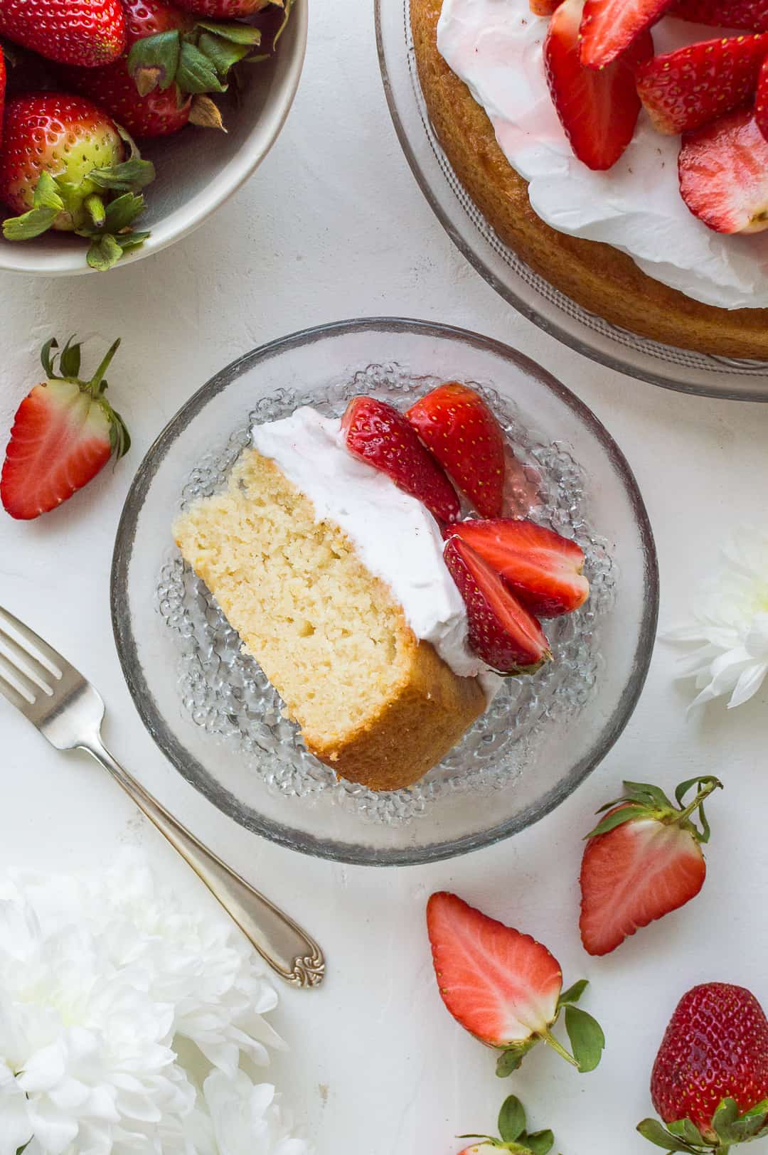 A top down shot of a slice of vegan lemon almond cake on a glass plate with strawberries