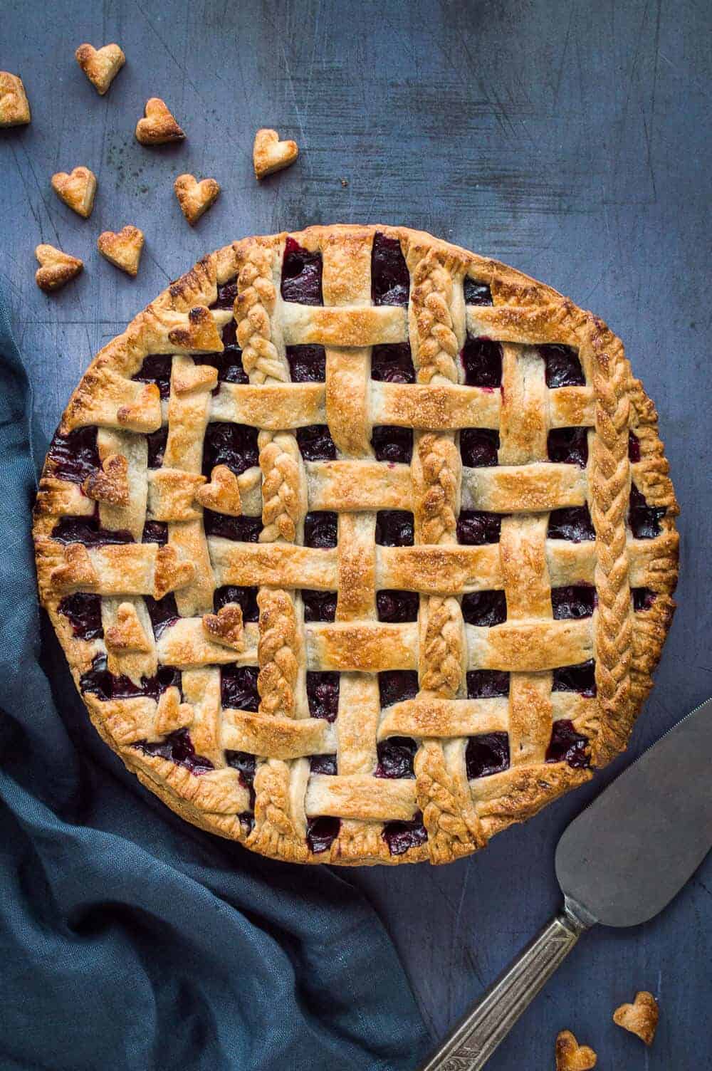 Unsliced baked vegan blueberry pie topped with a coconut oil pastry lattice and pastry braids and hearts.
