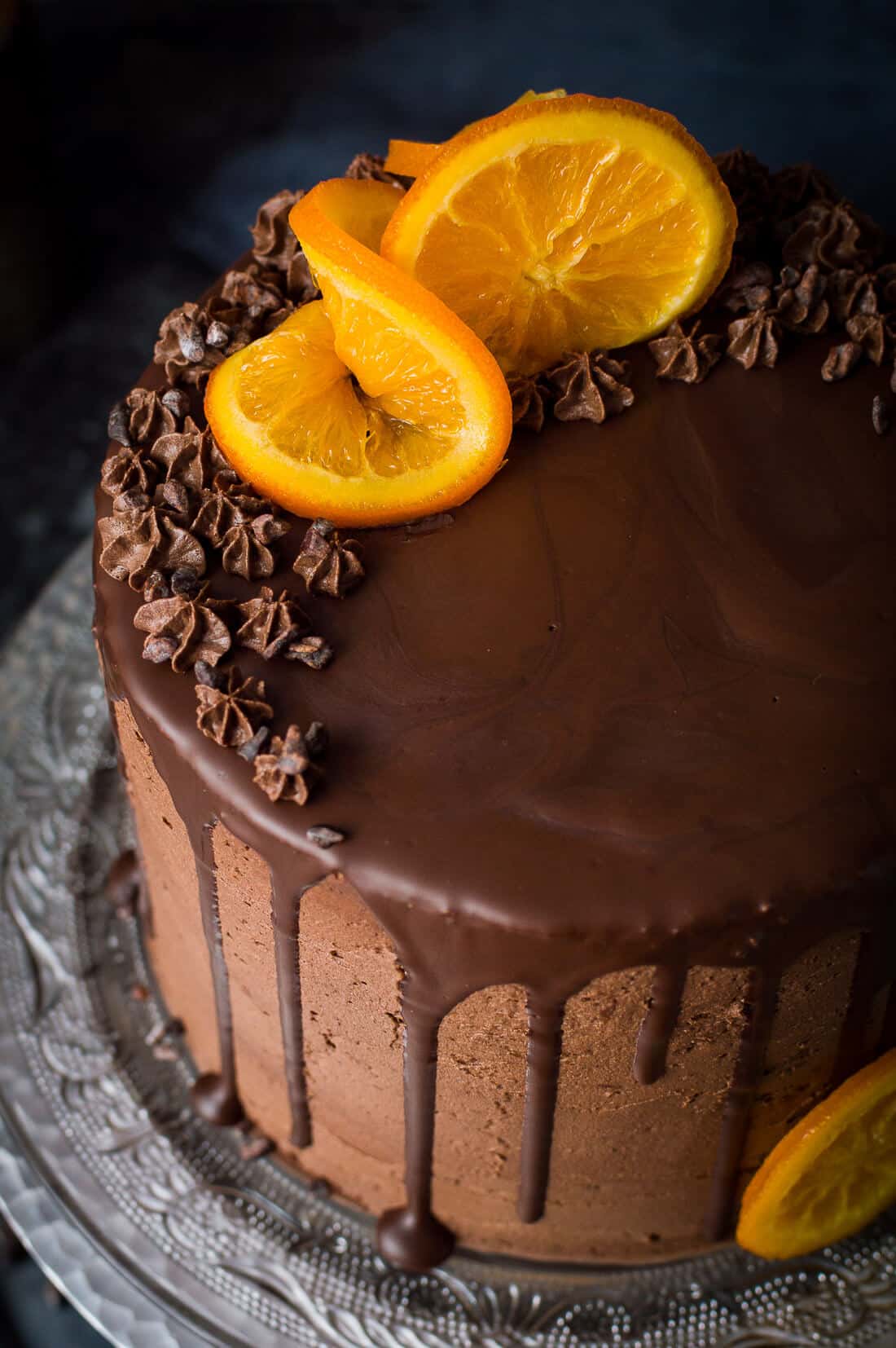 Close up of vegan orange and almond cake with chocolate buttercream, chocolate drip, candied oranges and cacao nibs.