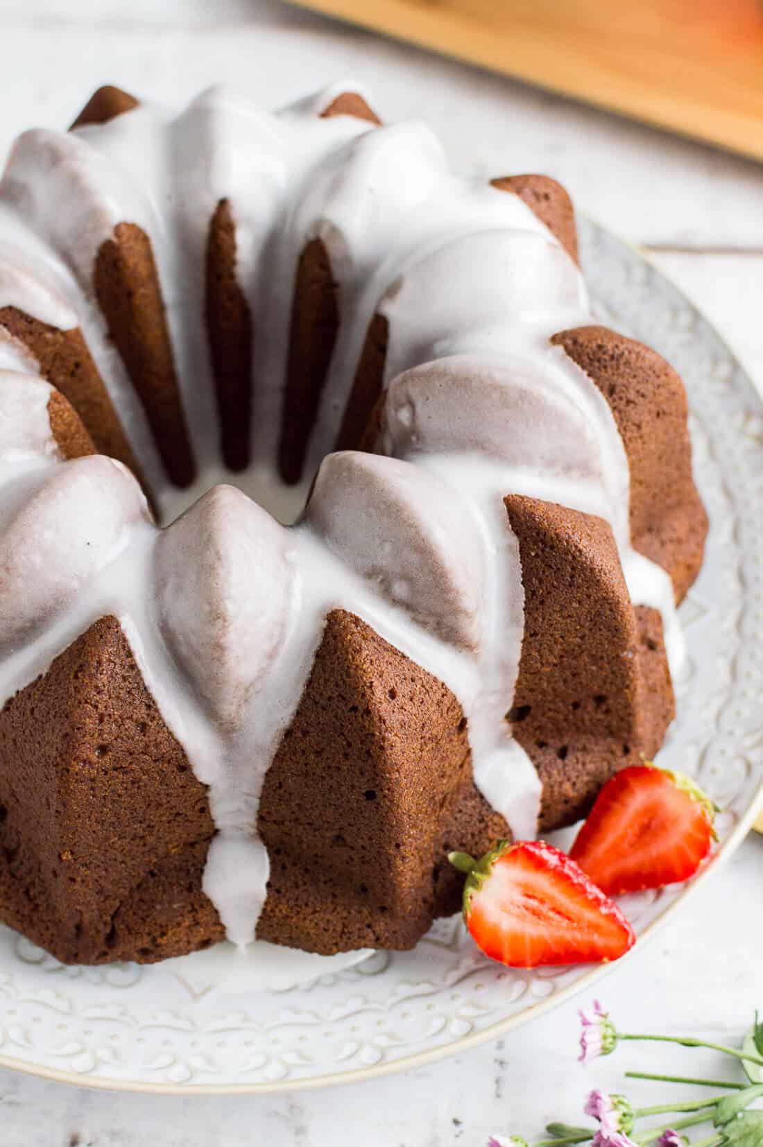 A close up of easy vegan gingerbread bundt cake with lime glaze and strawberries on a white plate and background.
