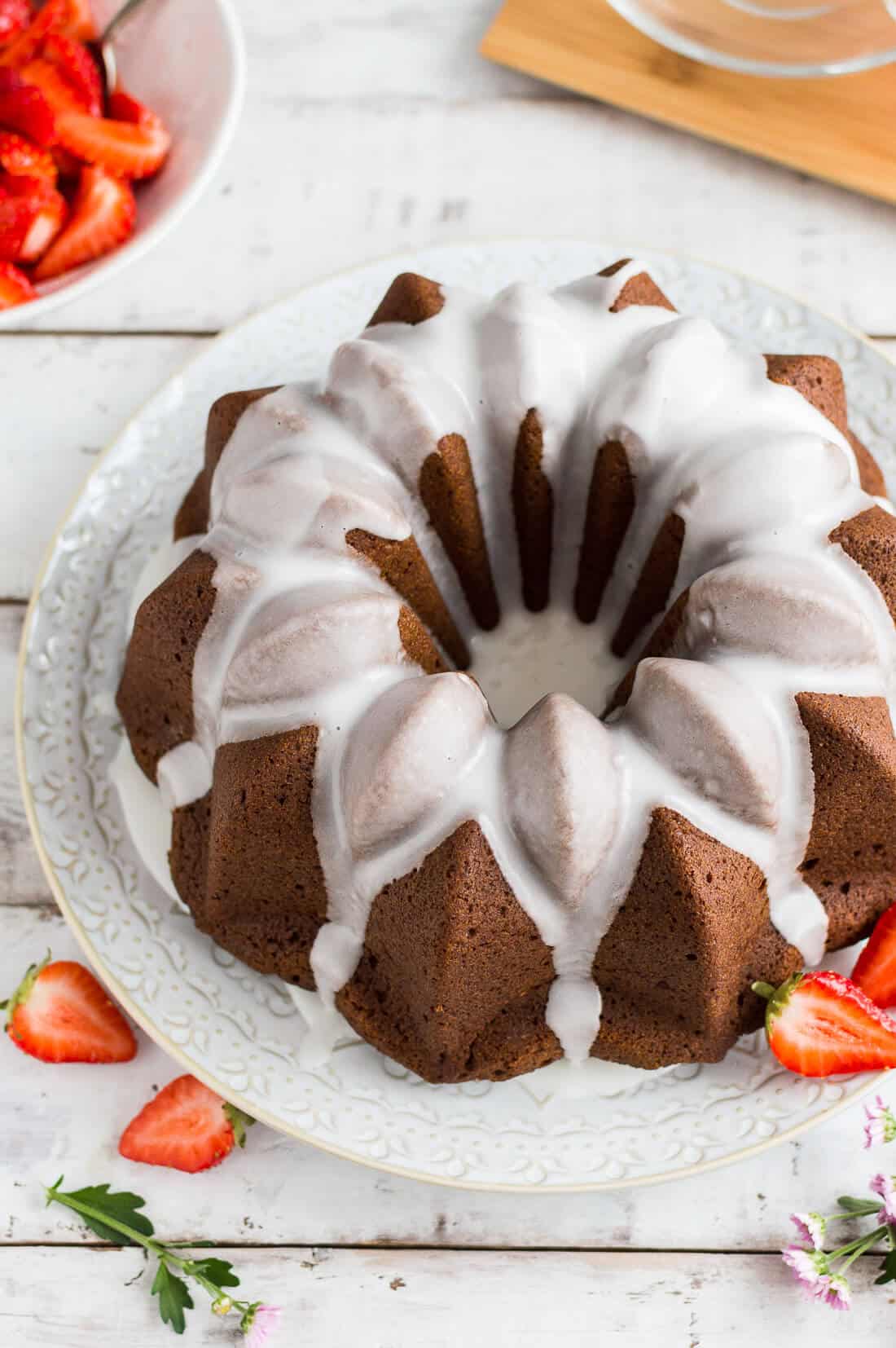 Side shot of vegan ginger bundt cake topped with a lime glaze and served with macerated strawberries.