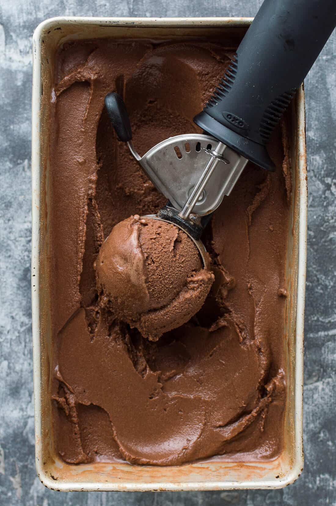 A tub of vegan chocolate coconut sorbet with an ice cream scoop.