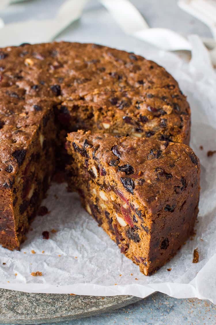 close up of a slice of vegan Christmas fruitcake on white baking parchment.