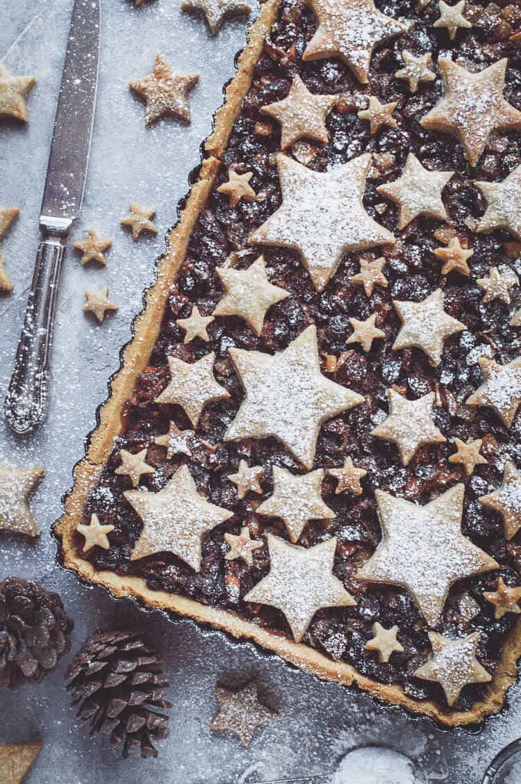 vegan shortbread star topped mince pie tart on agrey background with Christmas decorations.