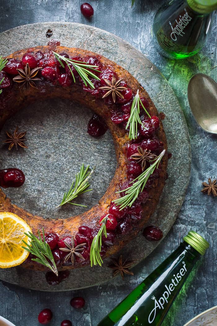 Close up of festive vegan nut roast topped with cranberry sauce, rosemary and spices with a bottle of Appletiser