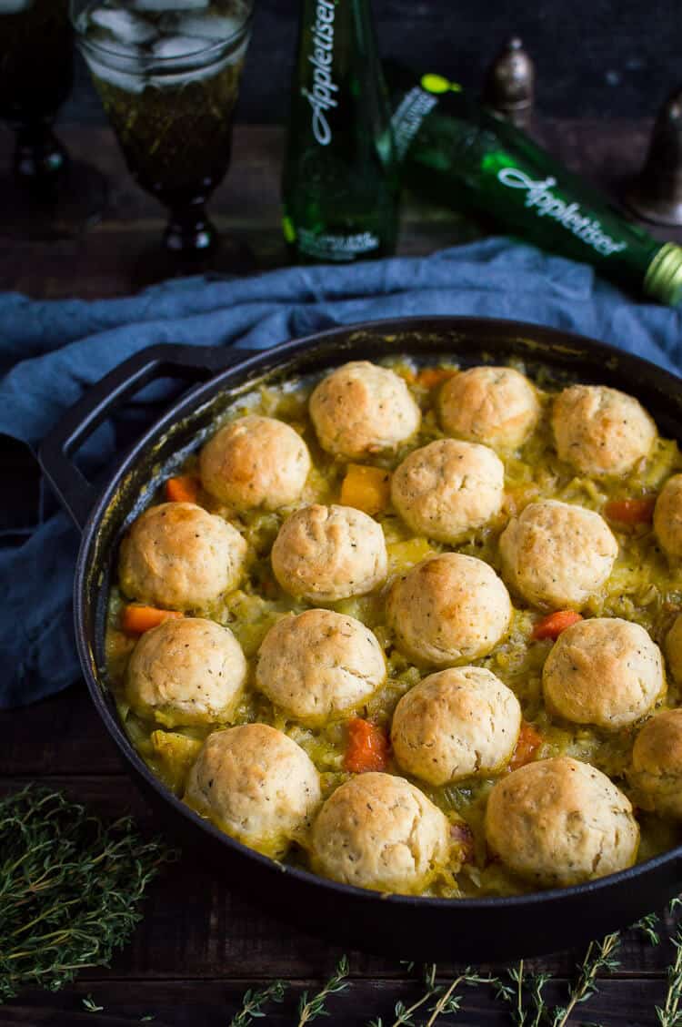 Vegan vegetable and pearl barley stew topped with herby dumplings in a cast iron pan with Appletiser in the background.