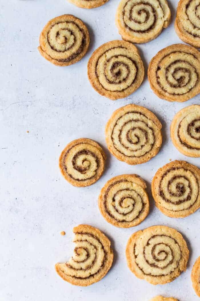Vegan cinnamon swirl cookies arranged on a grey background with a bite taken out of one.