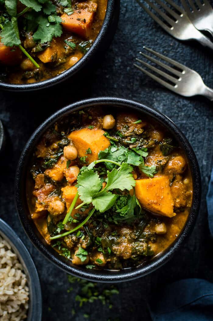 Close up of vegan chickpea, sweet potato and spinach curry in a black bowl on a black background.