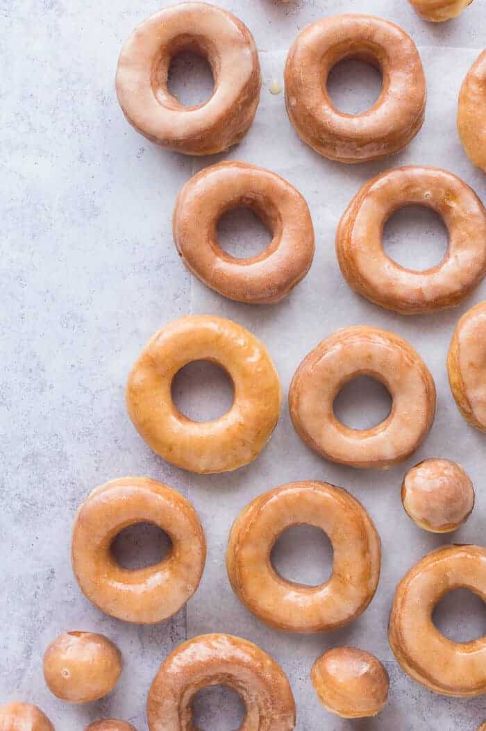 Vegan glazed doughnuts on a sheet of baking parchment on a grey background.