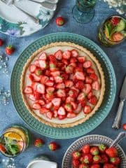 Vegan strawberry tart on a green platter with a bowl of strawberries and glasses of Pimms.