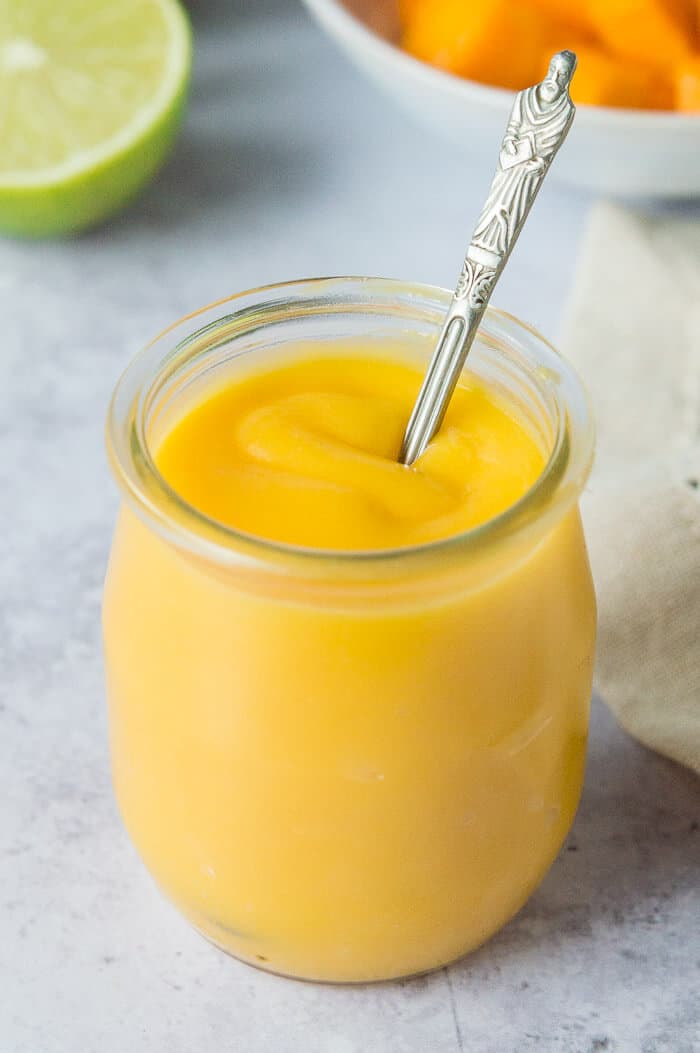 A small jar of mango curd with a teaspoon in it.
