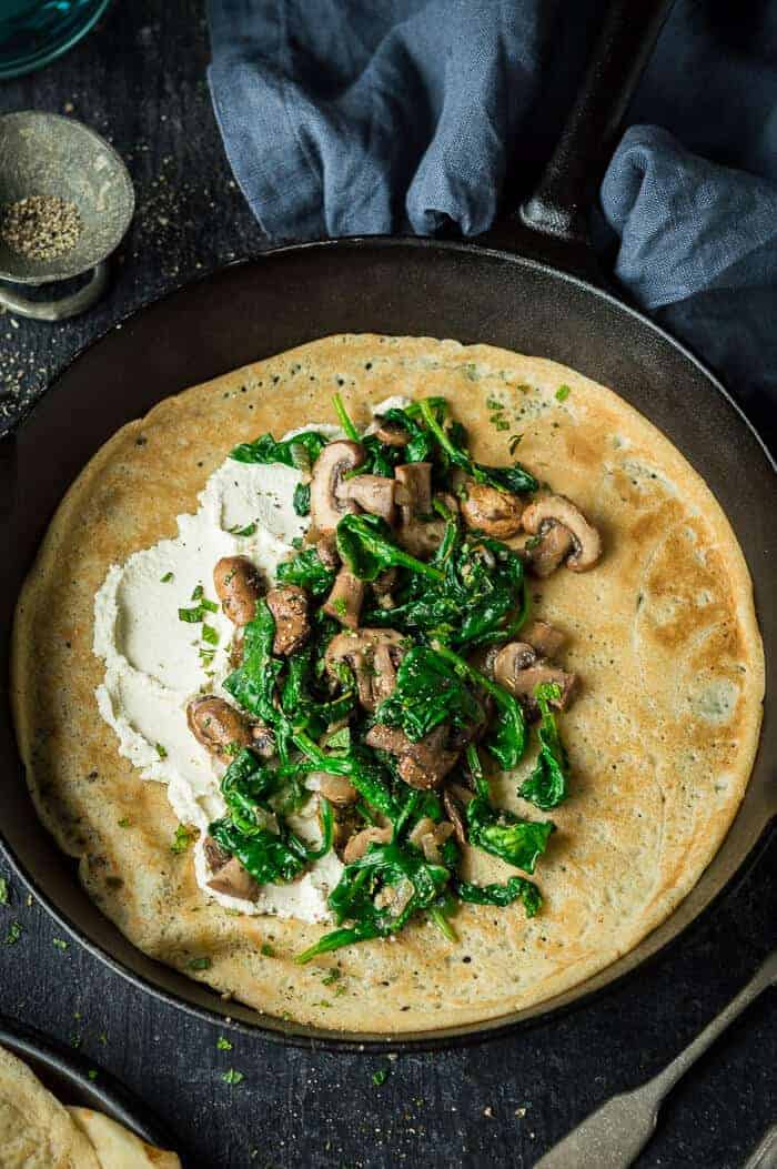 Vegan crepe topped with almond cheese, mushrooms and spinach in a cast iron pan.