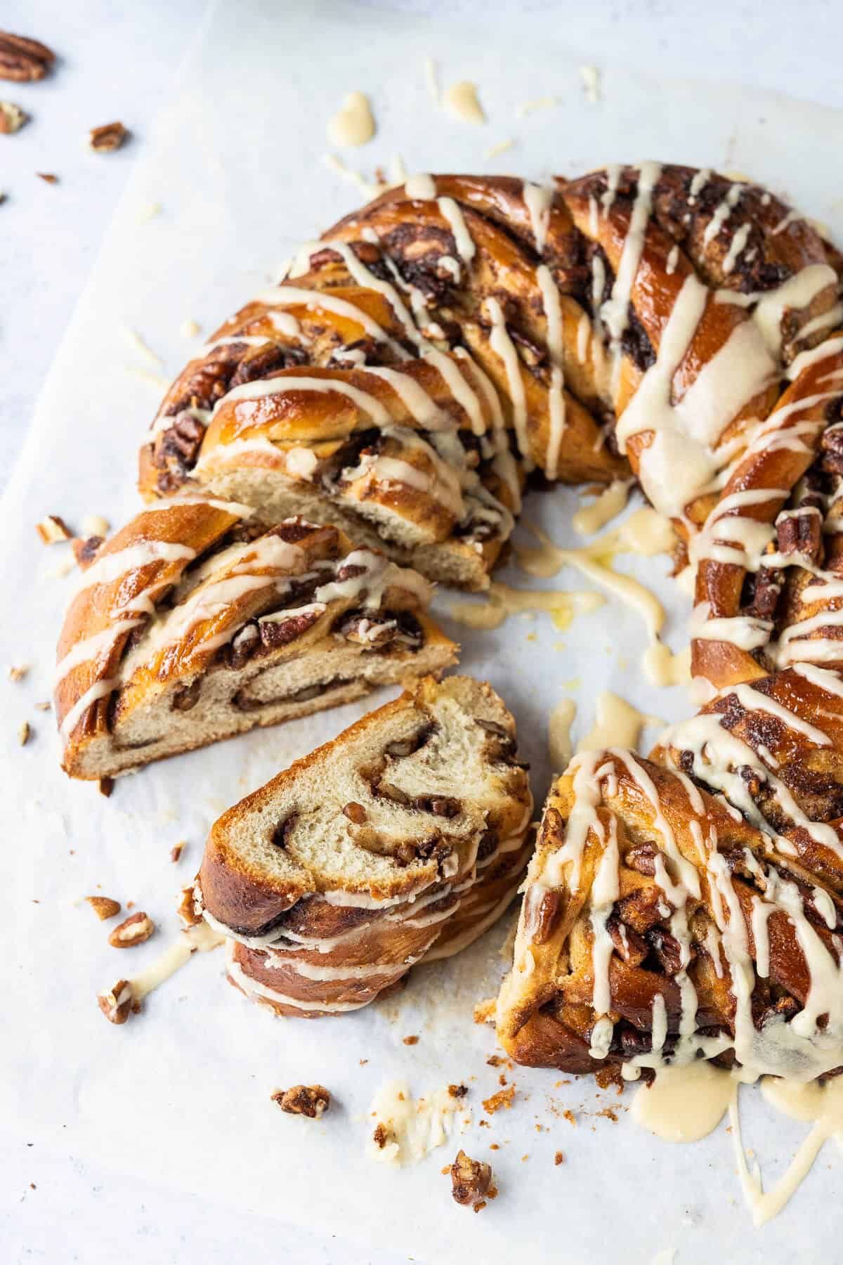 Close up of sliced maple pecan bread wreath drizzled with maple glaze on a sheet of baking parchment.