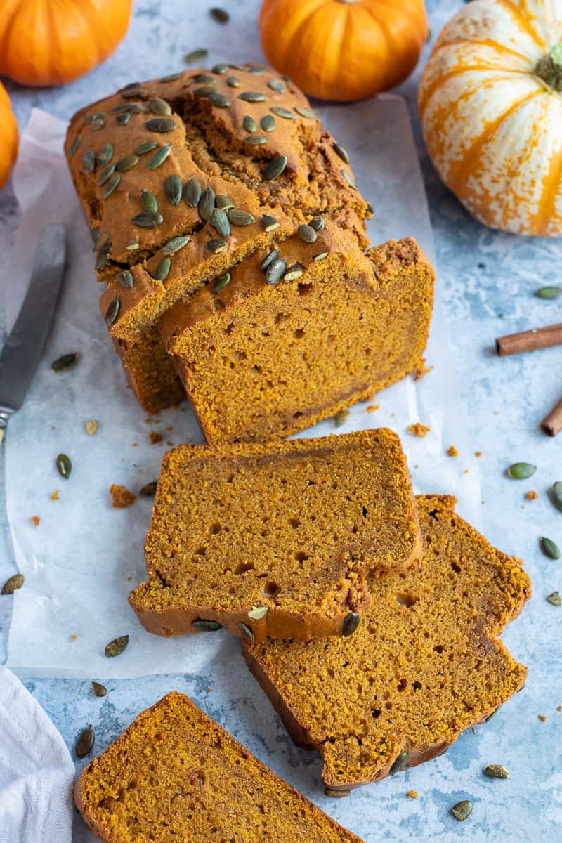 Sliced pumpkin bread loaf on a blue background with mini pumpkins.