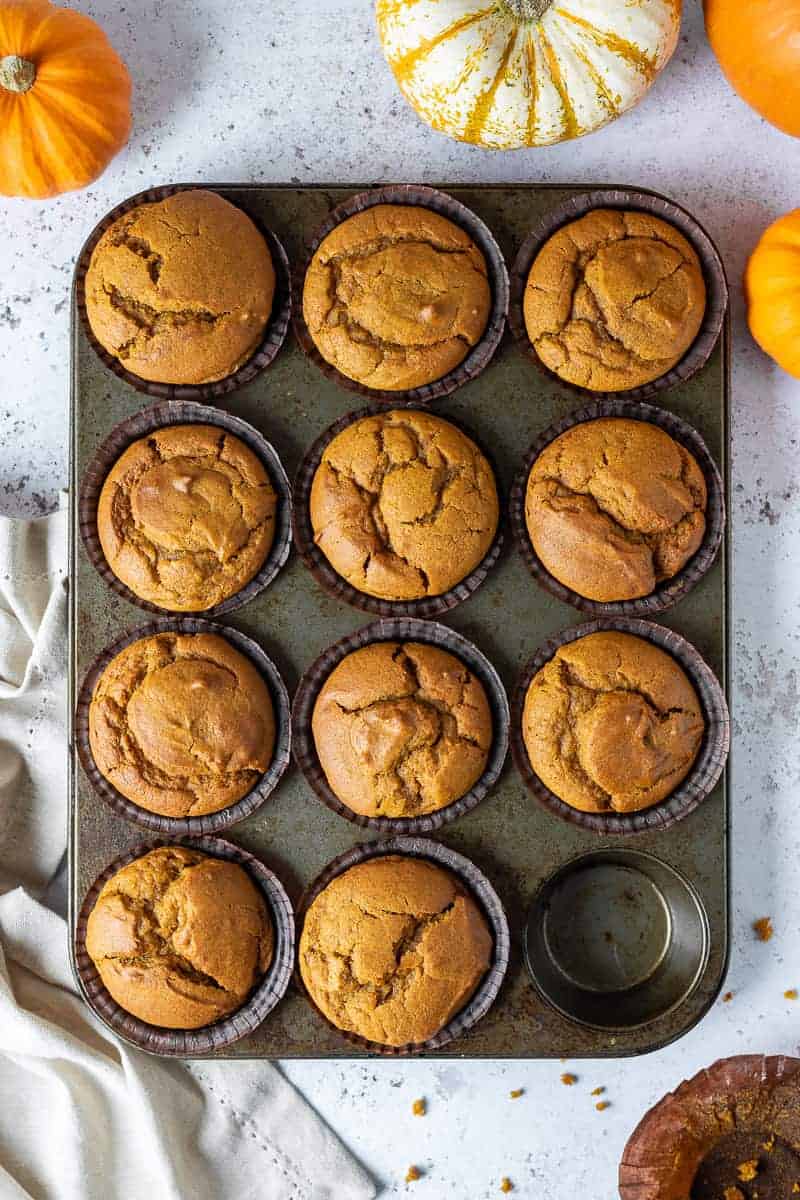 A tray of vegan pumpkin muffins on a white surface with mini fresh pumpkins.