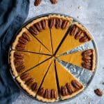 vegan pumpkin pie on a metal plate on a grey background with maple pecans.