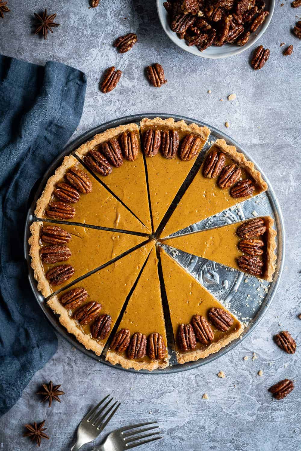 vegan pumpkin pie on a metal plate on a grey background with maple pecans.