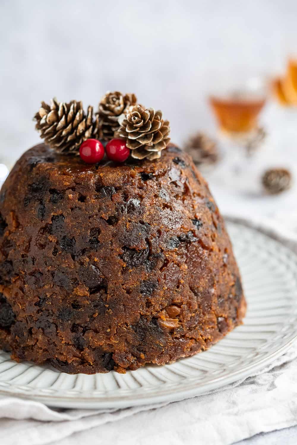 close up of vegan christmas pudding topped with pine cones and red berries.