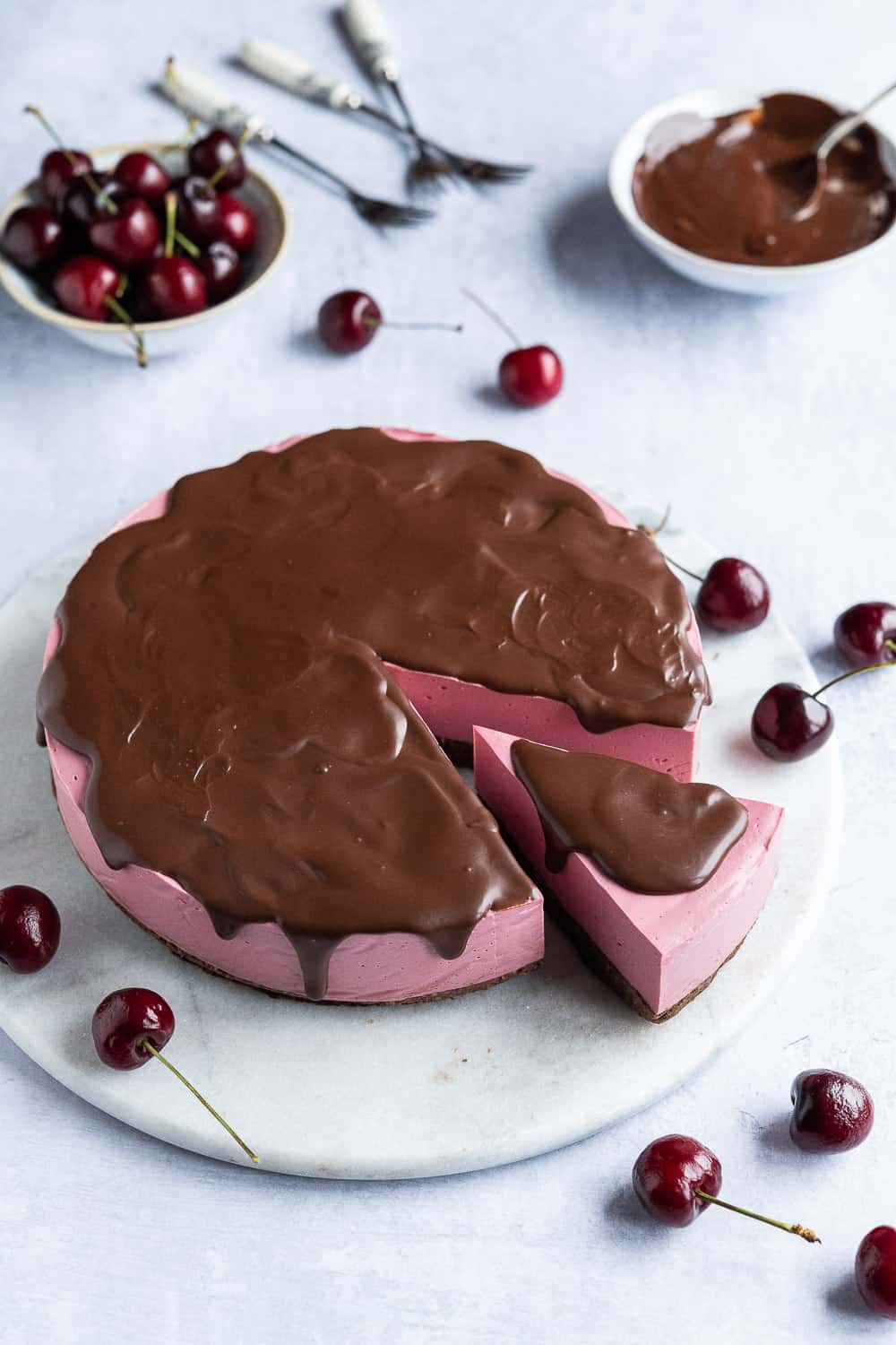 Cherry cheesecake with chocolate ganache and cherries on a marble platter.