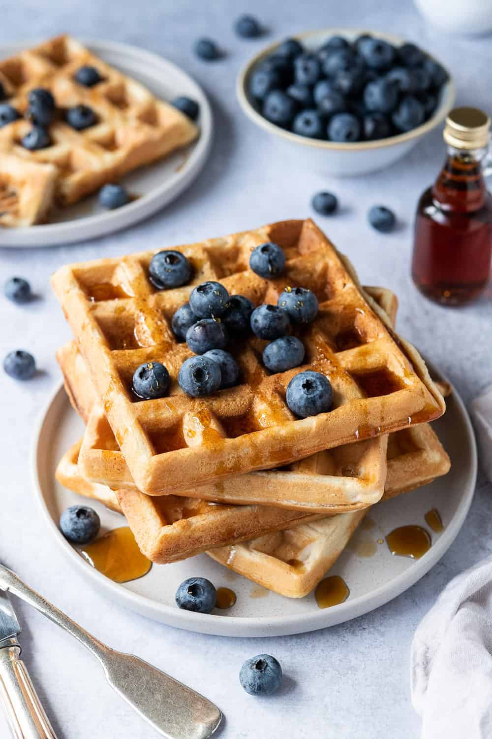 A stack of vegan waffles on a grey plate with blueberries and maple syrup.