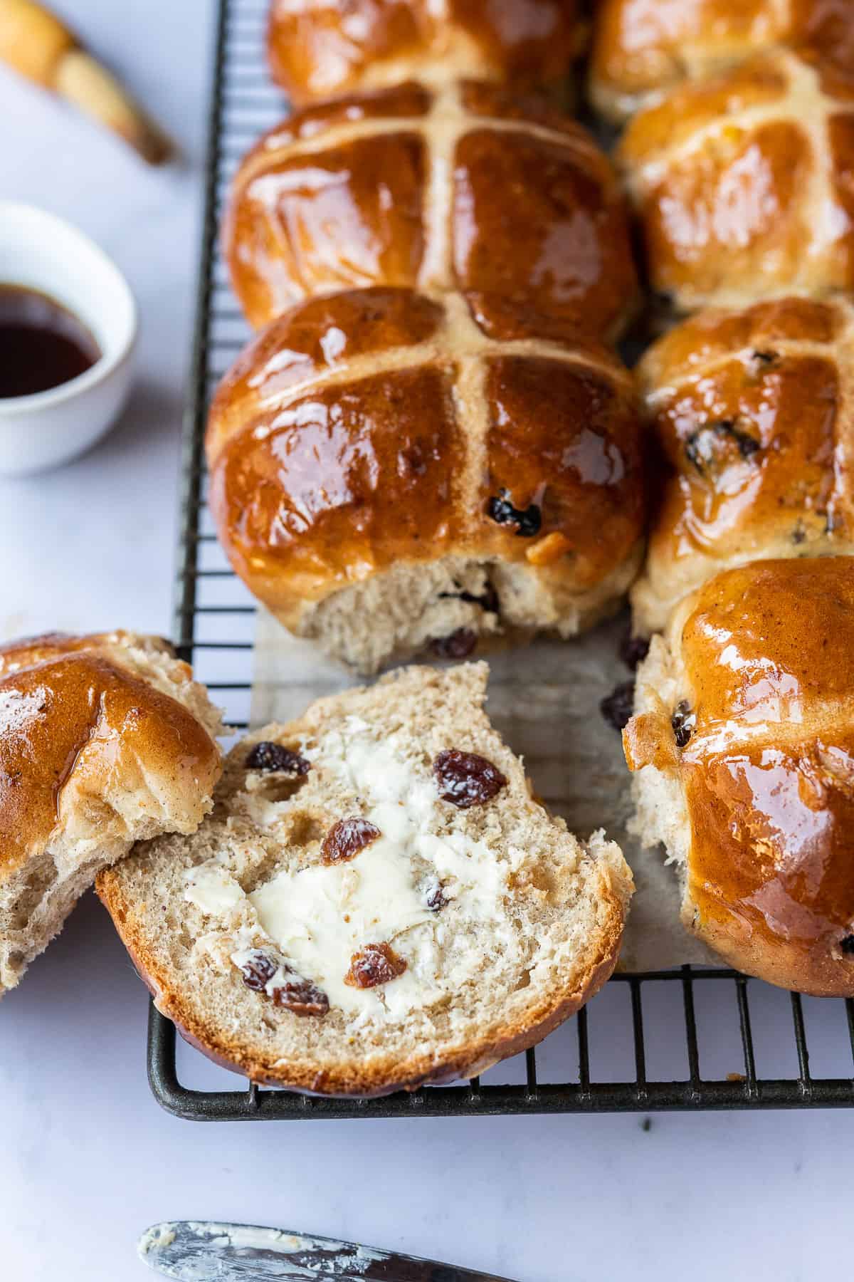 A hot cross bun sliced in half and spread with butter.