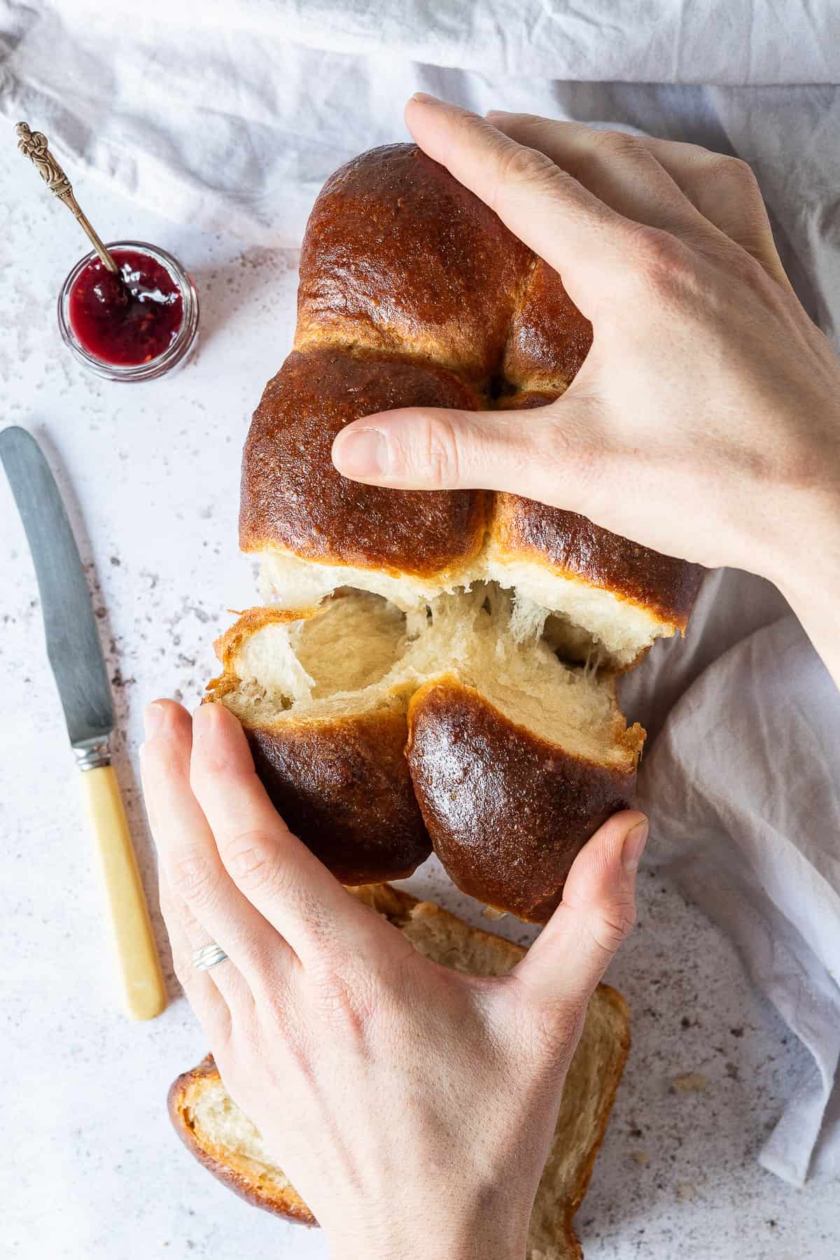 A loaf of brioche being torn apart by hands.