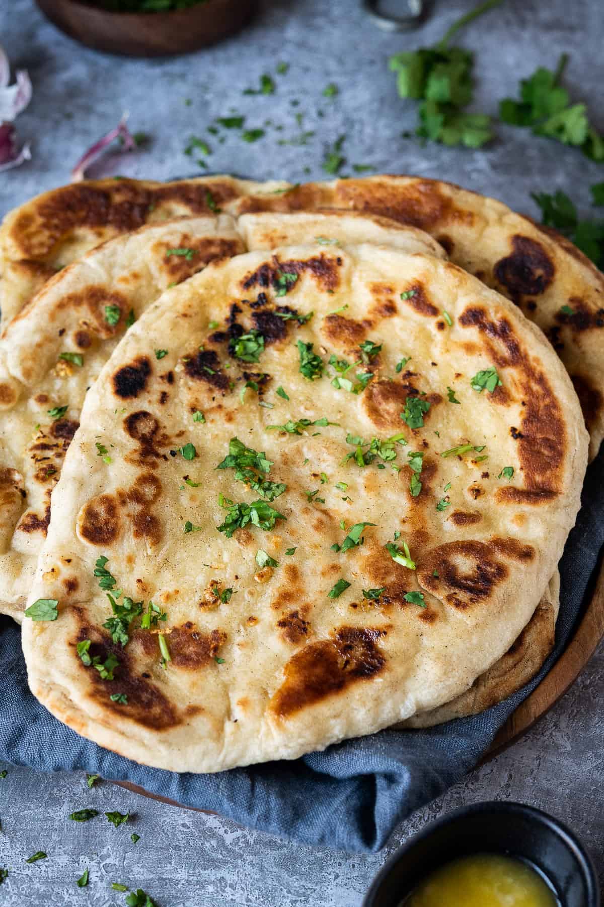 Vegan naan bread on a grey background with coriander and a bowl of garlic butter