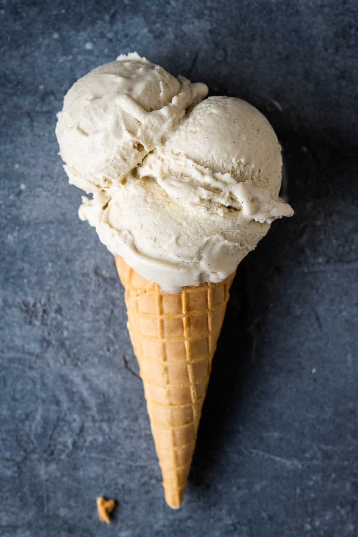 A waffle cone with three scoops of ice cream on a grey background.