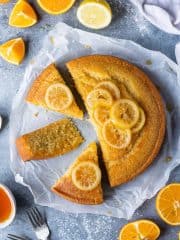 Vegan semolina cake cut into slices on a sheet of baking parchment on a grey background with sliced oranges and lemons