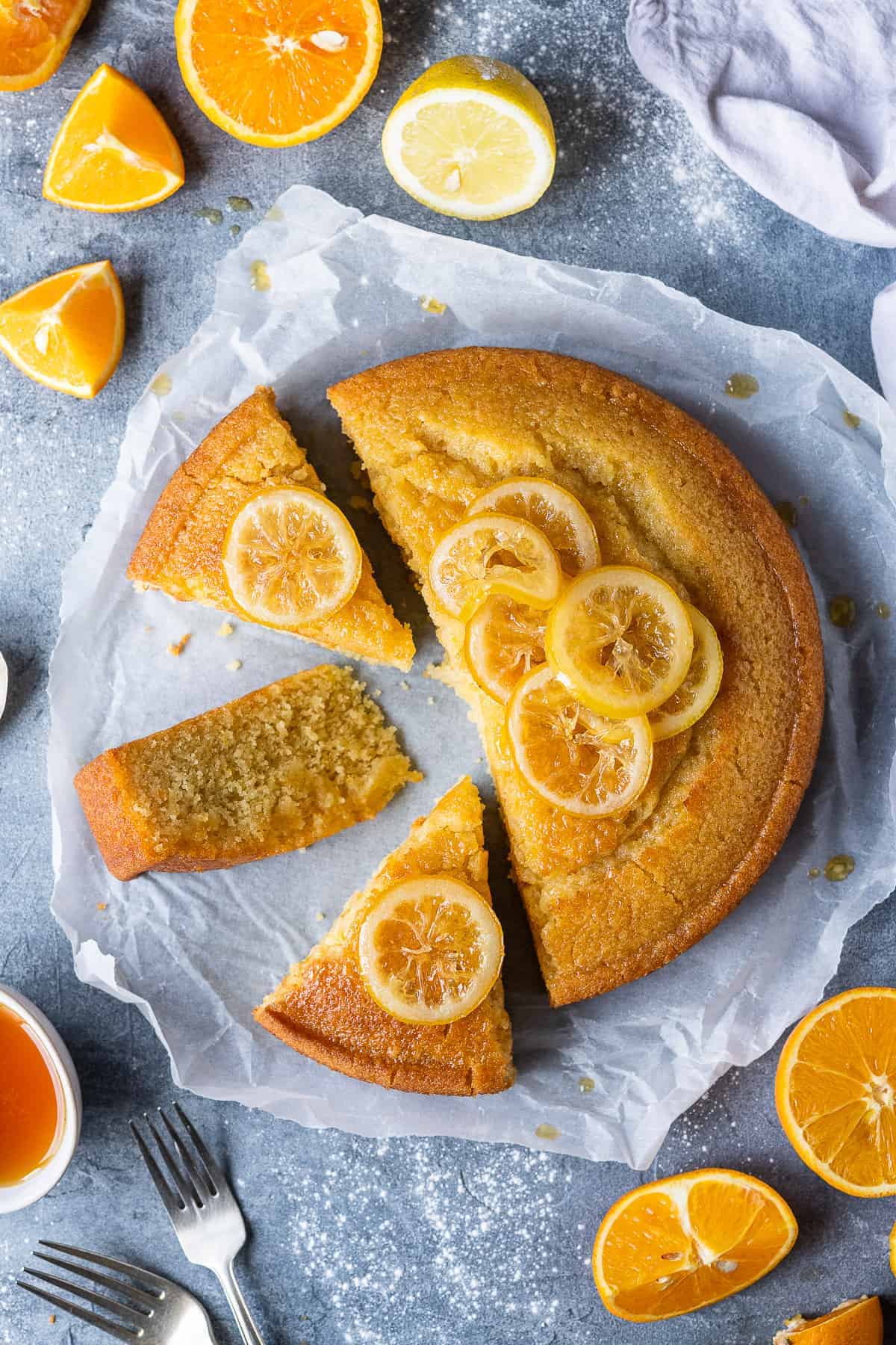Vegan semolina cake cut into slices on a sheet of baking parchment on a grey background with sliced oranges and lemons