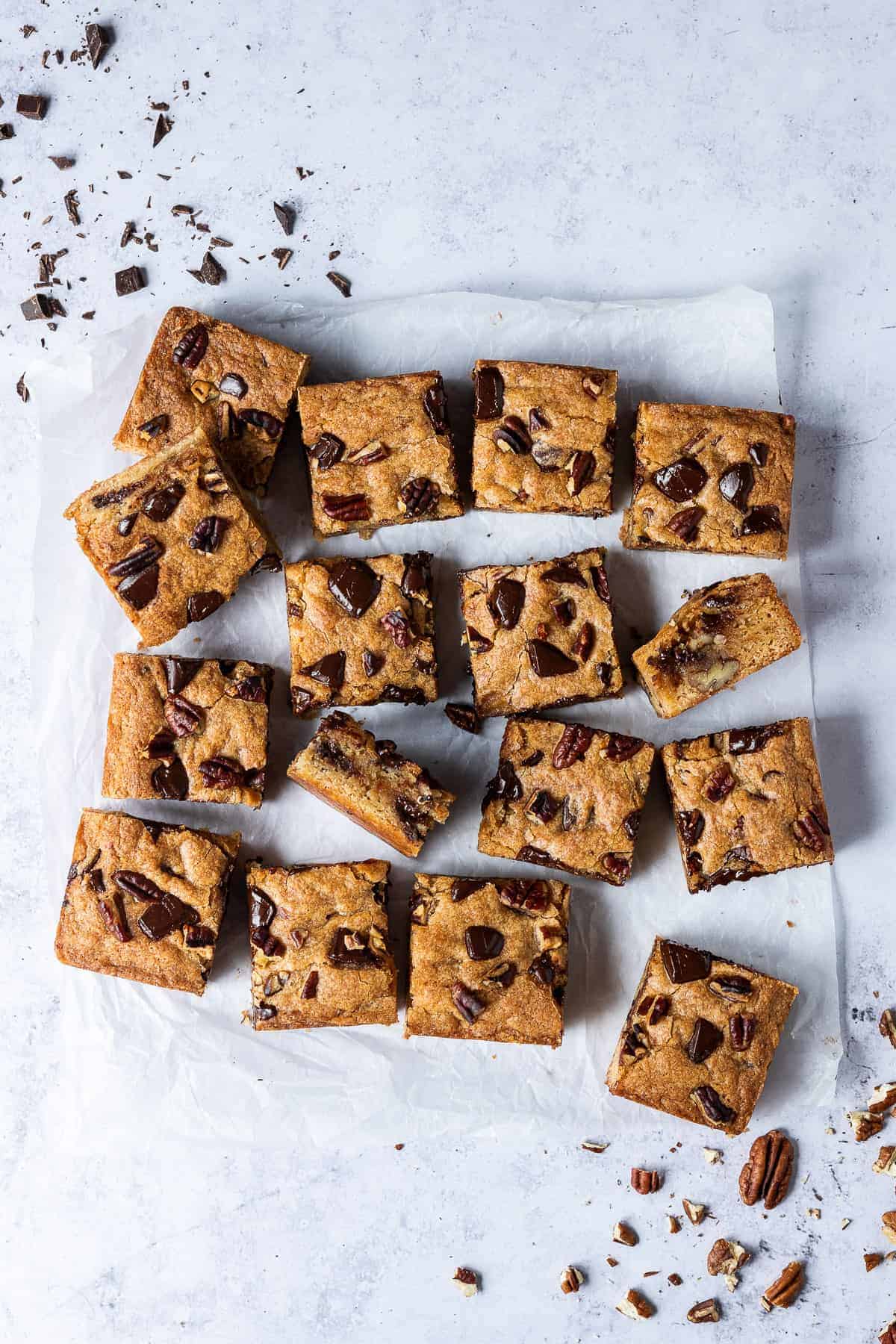 Vegan banana blondies cut into squares on a grey background with chopped pecans and chocolate.