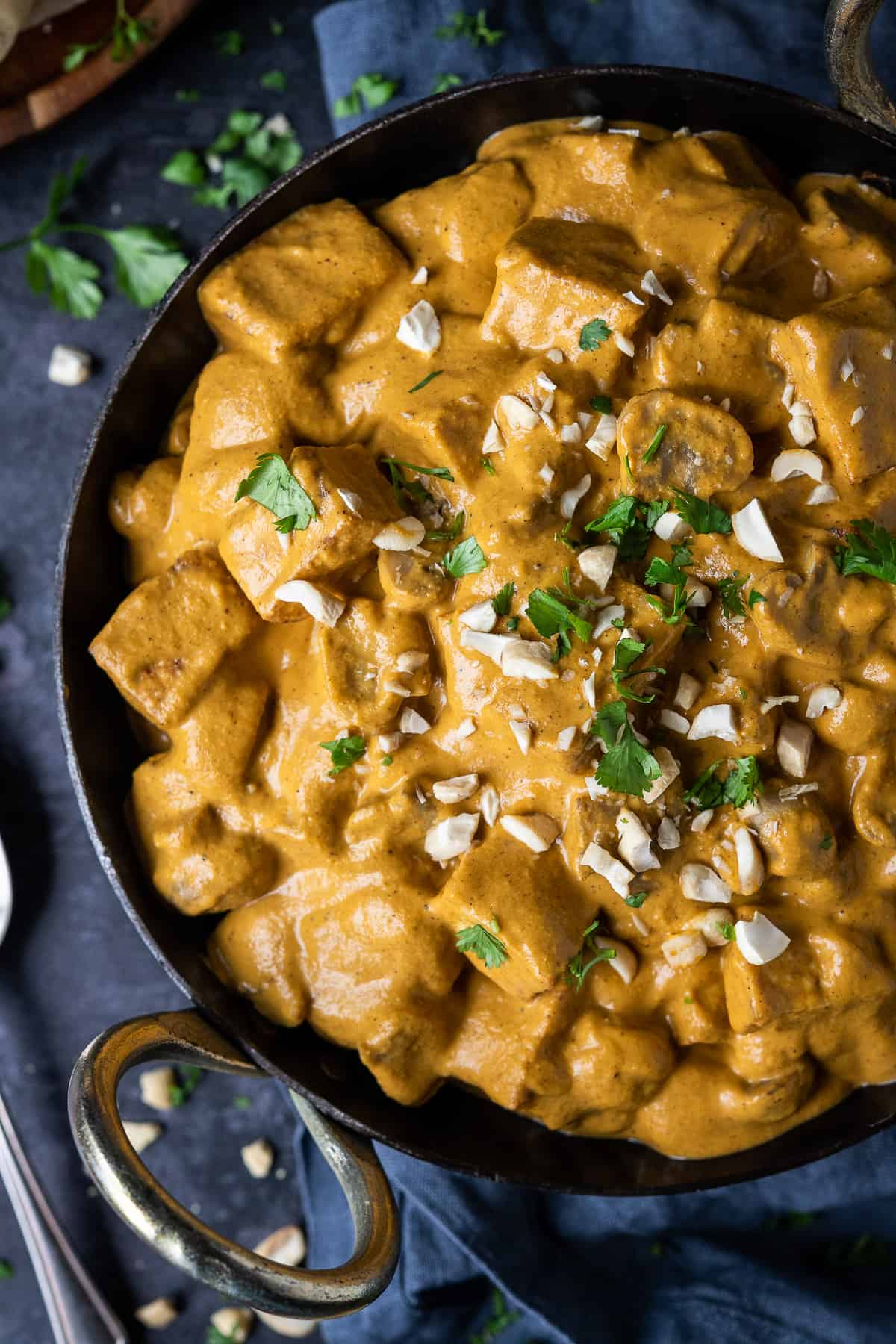 Close up of vegan korma in a black pan topped with chopped cashews and coriander.