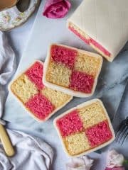 Three slices of vegan Battenberg cake on a marble board with fresh roses and a cup of tea.