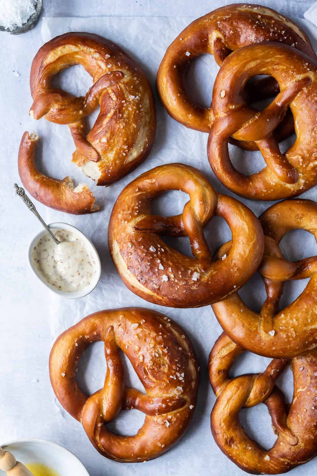 Vegan beer pretzels on a sheet of white baking parchment with a bowl of mustard sauce.