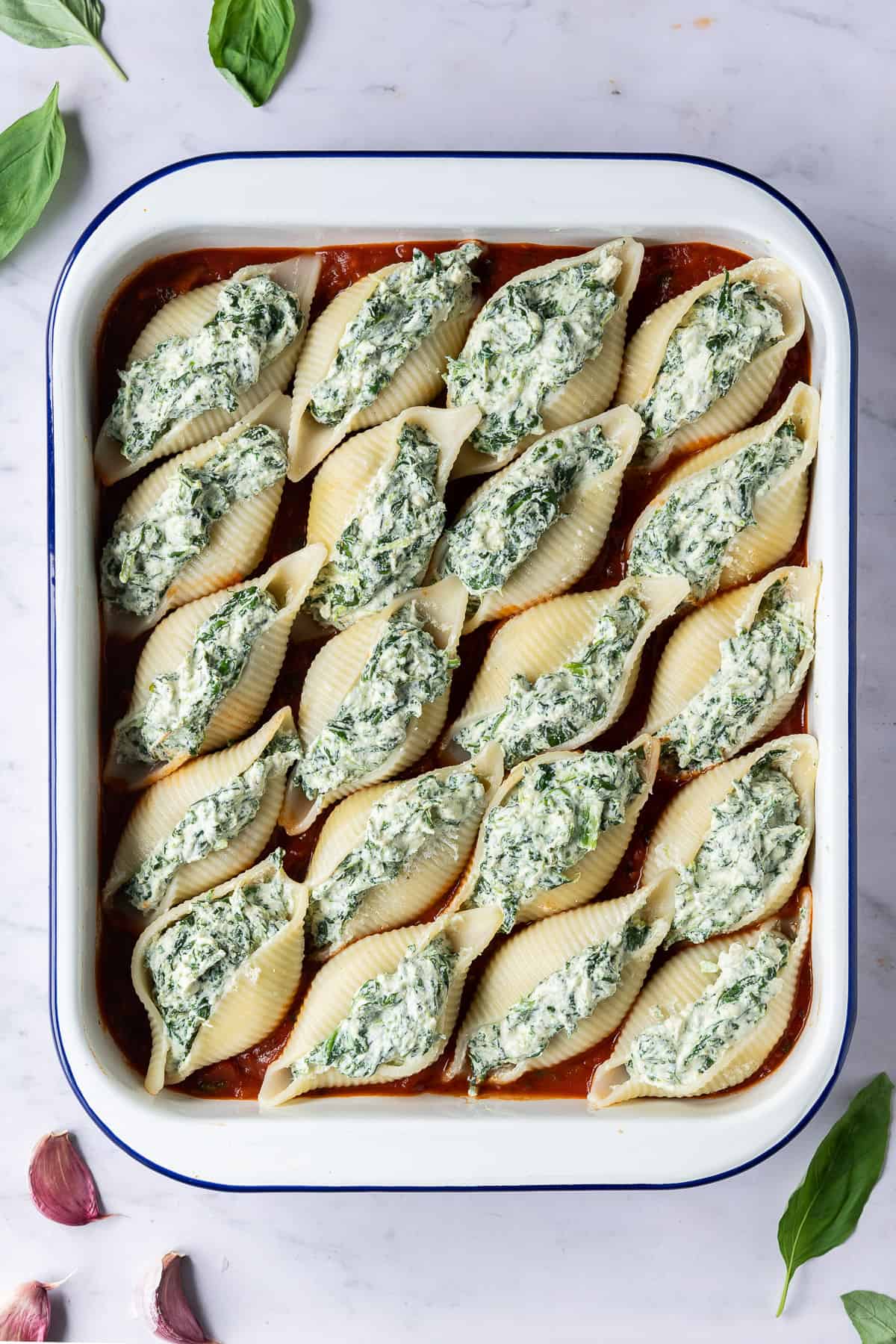 A dish of unbaked vegan spinach and ricotta stuffed pasta shells.