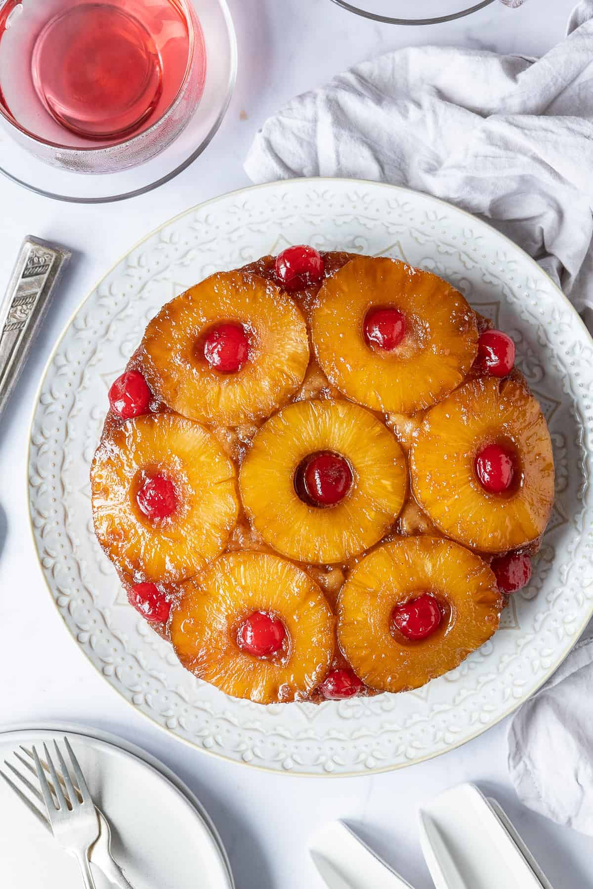 Vegan pineapple upside-down cake on a white plate on a marble background with a cup of fruit tea, plates and a grey cloth.