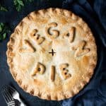 Chickpea, leek and mushroom pie with the words "vegan pie" written on top, on a dark background with forks, parsley, salt and pepper shakers and a grey cloth.
