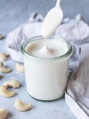 A jar of cashew cream with a spoon being dipped in.