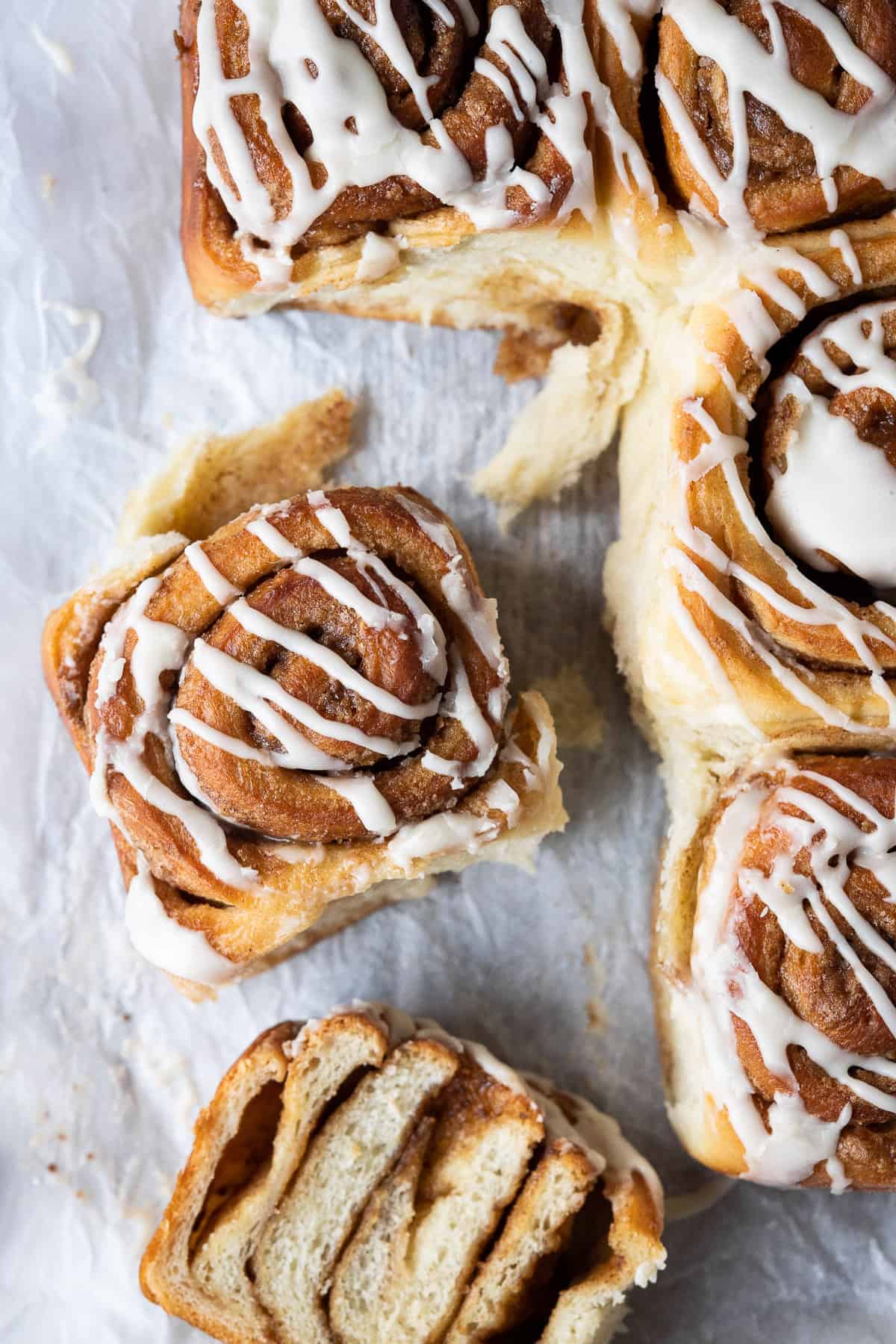 Cinnamon rolls on white baking parchment, one sliced in half.