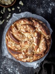 Almond bread twist on white baking parchment on a wooden table with a bowl of flaked almonds.