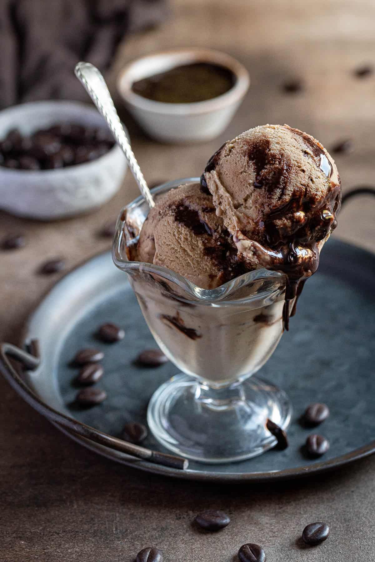 Two scoops of vegan coffee ice cream in a glass on a metal tray.