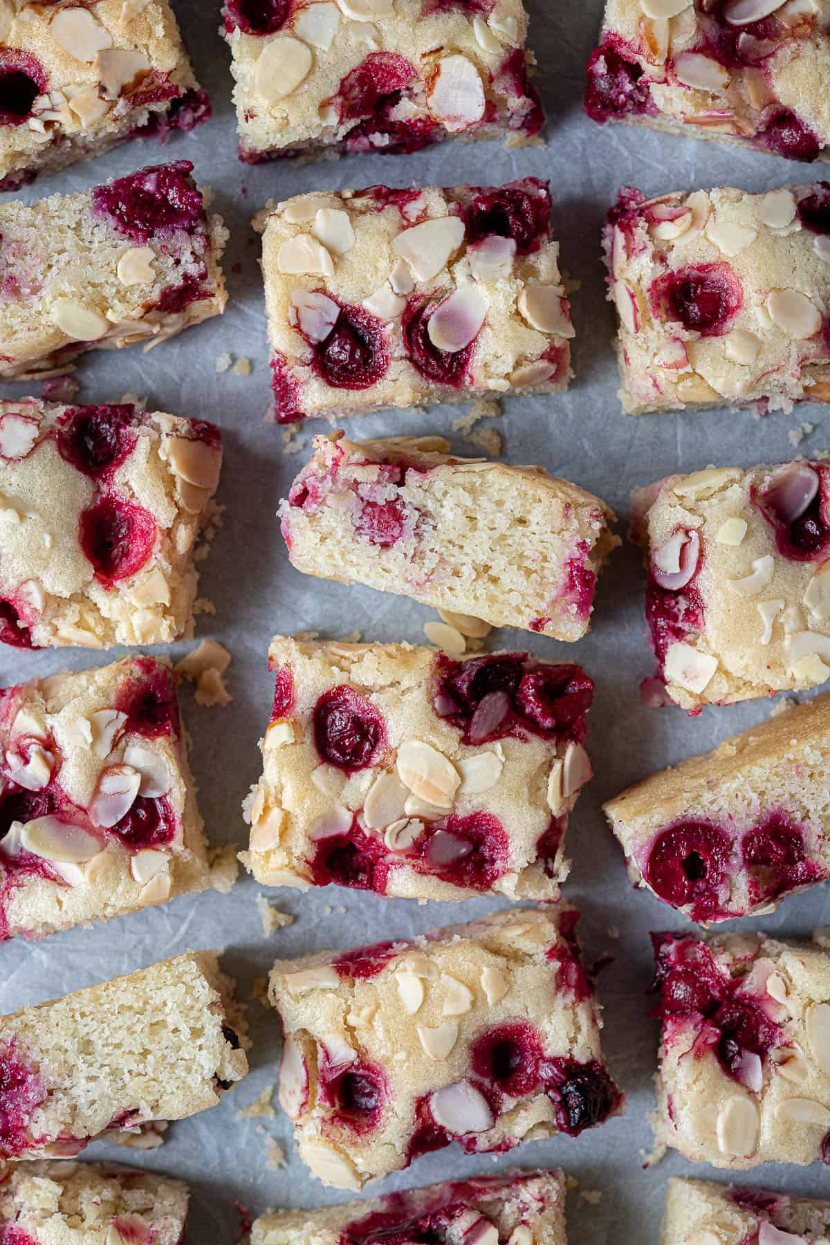 Squares of vegan cherry almond cake on baking parchment.
